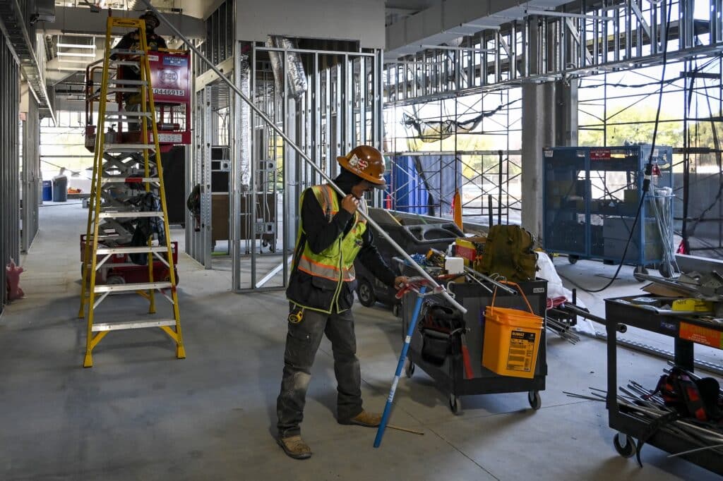 An electrical contractor in Boise, Idaho, bends conduit with a blue tool inside a partially built site amid tools and building supplies.